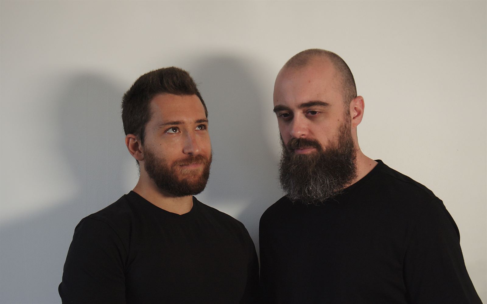 Ben C and Kalsx in black t-shirts against a light wall